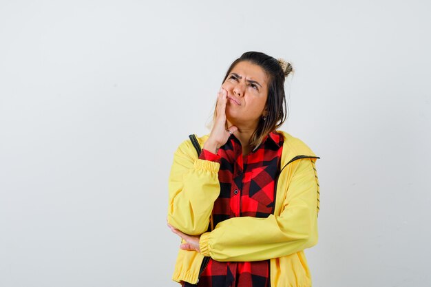 Mooie vrouw in shirt, jas met hand op de wang, omhoog kijkend en peinzend kijkend, vooraanzicht.