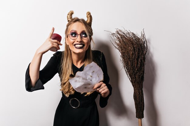 Mooie vrouw in vampierkostuum die pret in halloween hebben. Blije jonge heks die gezichten op witte muur maakt.