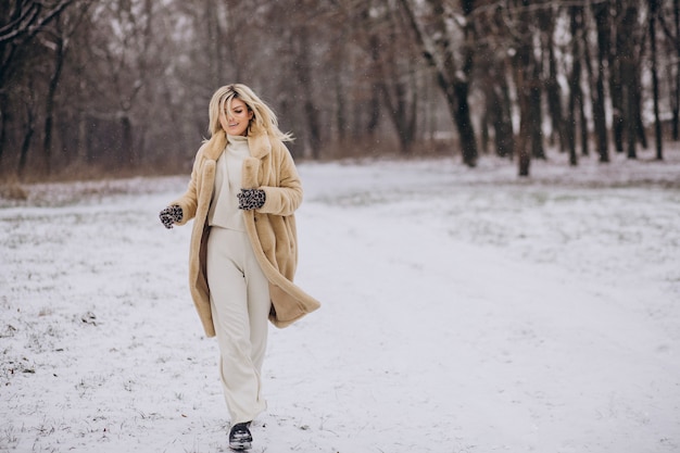 Mooie vrouw in winterjas wandelen in park vol sneeuw