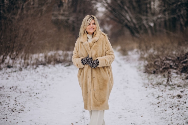 Mooie vrouw in winterjas wandelen in park vol sneeuw