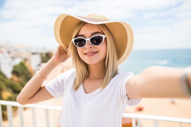 Mooie vrouw in zonnebril en zomerhoed die selfie op strand nemen