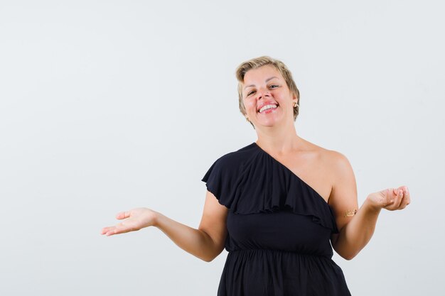 Mooie vrouw in zwarte blouse die open palm uitspreidt die opzij iets tonen en gelukkig kijken