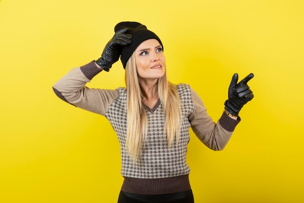 Mooie vrouw in zwarte handschoenen en hoed staande op geel.