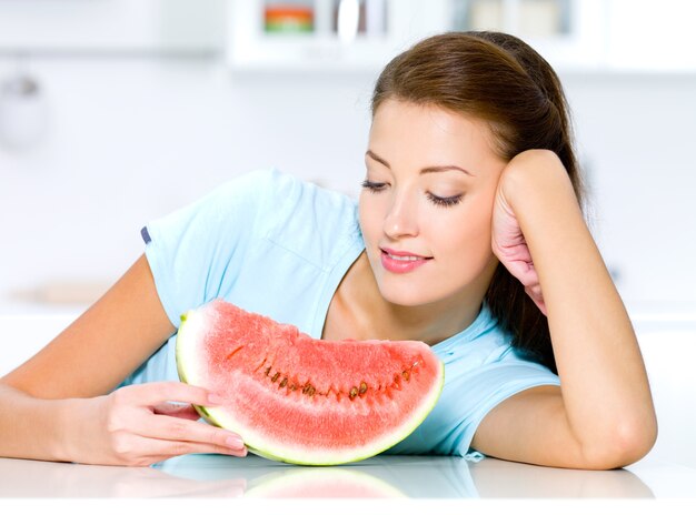Mooie vrouw kijkt naar een rode watermeloen in de keuken
