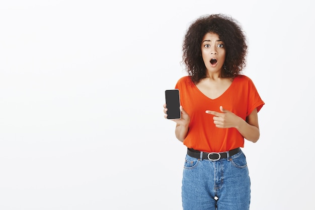 Mooie vrouw met afro kapsel poseren met haar smartphone in de studio