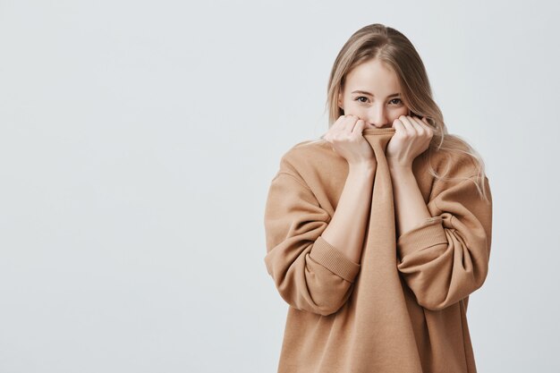 Mooie vrouw met blond steil haar en donkere aantrekkelijke ogen die haar gezicht verbergen in een warme, losse trui.