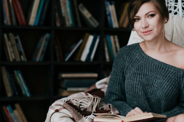 Mooie vrouw met boek in leunstoel dichtbij boekenrekken