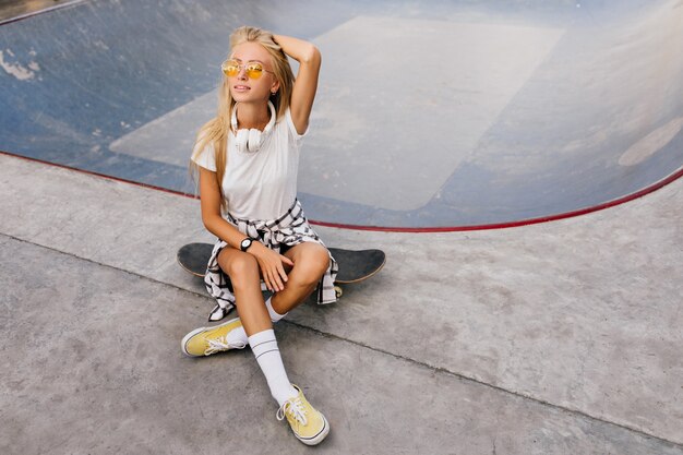 Mooie vrouw met een gebruinde huid zittend op een skateboard en spelen met blonde haren.