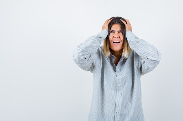 Mooie vrouw met handen op het hoofd in overhemd en bedroefd kijken, vooraanzicht.