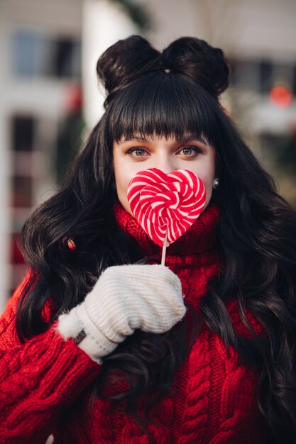 Mooie vrouw met kapsel in rode trui en wanten met lolly voor mond.