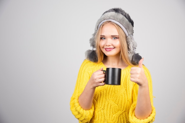 Mooie vrouw met kopje thee duimen opgevend.