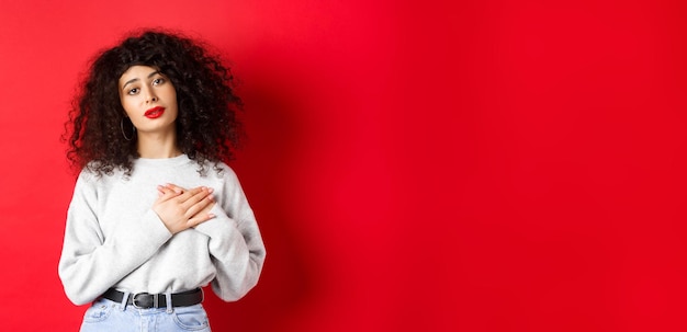 Mooie vrouw met krullend haar die zich aangeraakt voelt en dankbaar hand in hand op het hart houdt en meekijkt