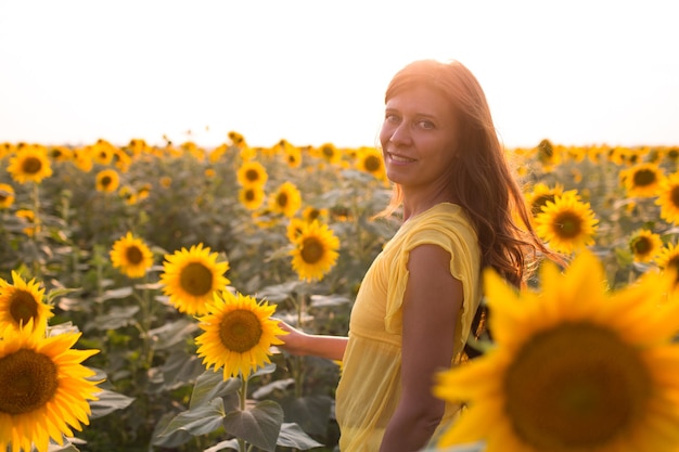 Mooie vrouw met lang haar in witte jurk in een veld met zonnebloemen in de zomer in het zonlicht