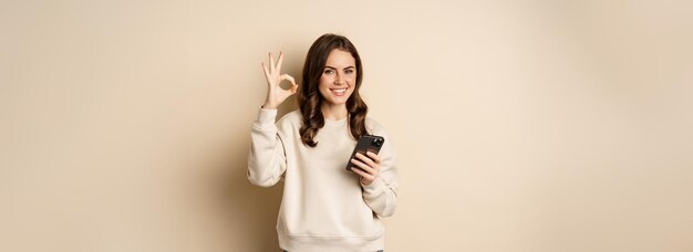 Mooie vrouw met mobiele telefoon en ok teken die toepassingswinkel-app s aanbeveelt