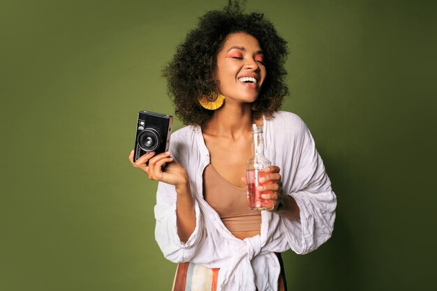 Gratis foto mooie vrouw met strak kapsel poseren met camera en limonade drinken