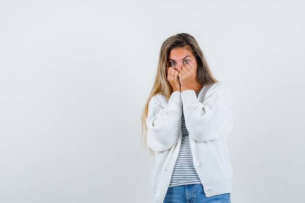 Mooie vrouw met vuisten op gezicht in jasje, t-shirt en op zoek overweldigd, vooraanzicht.