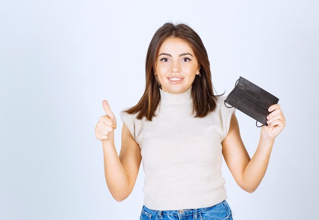 Mooie vrouw met zwart medisch masker die een duim toont.