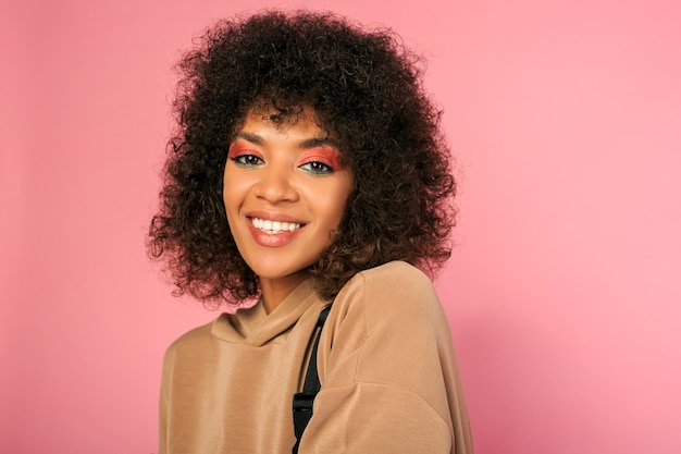 Mooie vrouw met zwarte huid en stijlvol afrikaans kapsel in sportieve outfit poseren op roze