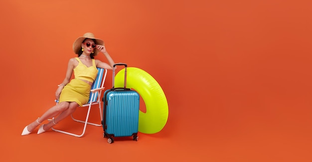 Mooie vrouw ontspannen zittend op een strandstoel met koffer en rubberen ring in studio zomer