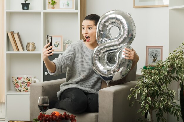 Mooie vrouw op gelukkige vrouwendag met nummer acht ballon zittend op een fauteuil in de woonkamer