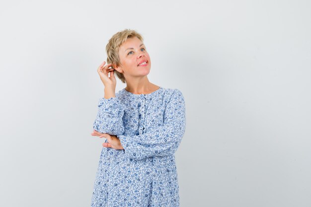 Mooie vrouw poseren met hand aanraken horen in blouse met patroon en op zoek charmant, vooraanzicht.