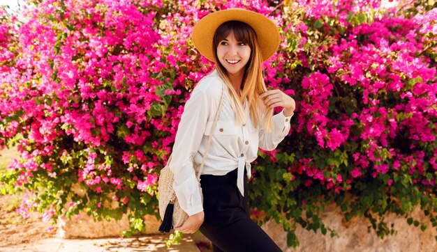 Mooie vrouw staande op roze bloemen dragen strooien hoed en casual outfit.