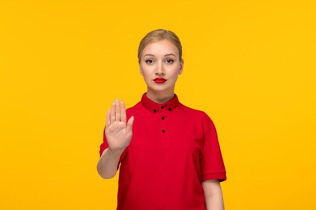 Mooie vrouw van de rode overhemddag die stopgebaar in een rood overhemd op een gele achtergrond toont