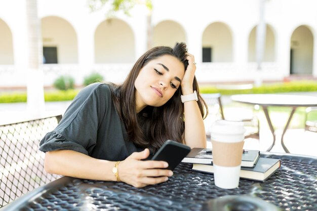 Mooie vrouw verveeld met online inhoud op mobiele telefoon aan tafel in de tuin