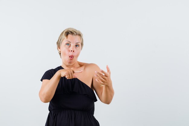 Mooie vrouw wijzend op iets op mobiele telefoon in zwarte blouse en op zoek met stomheid geslagen