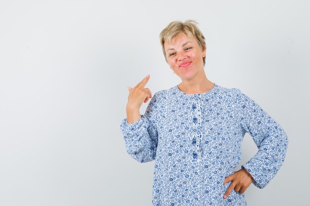 Mooie vrouw wijzend op zichzelf in blouse met patroon en op zoek zelfverzekerd. vooraanzicht. ruimte voor tekst