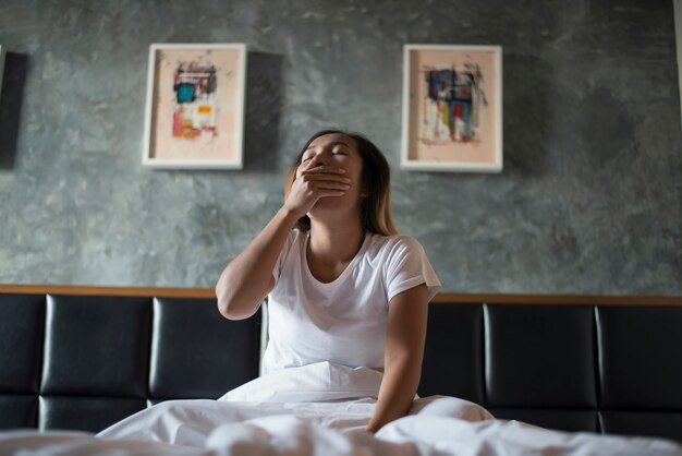 Mooie vrouw zittend op het bed en geeuwen in de slaapkamer