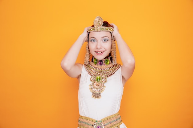 Mooie vrouw zoals cleopatra in oud egyptisch kostuum blij en opgewonden hand in hand op haar hoofd op sinaasappel
