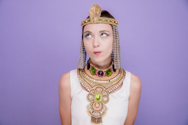 Mooie vrouw zoals cleopatra in oud egyptisch kostuum opzoeken met peinzende uitdrukking denkend aan paars