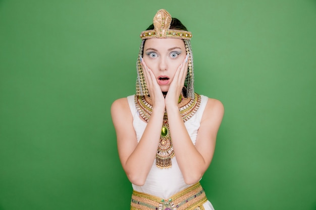 Mooie vrouw zoals cleopatra in oud egyptisch kostuum verbaasd en verrast op groen Premium Foto