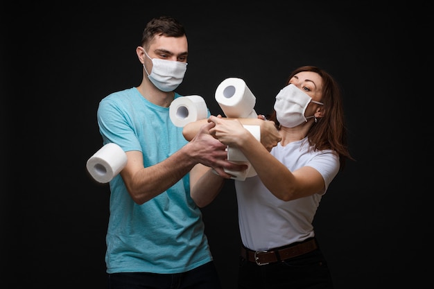 Mooie vrouwelijke en knappe man staat dicht bij elkaar in een witte en blauwe t-shirts en witte medische maskers en vecht voor veel wc-papier