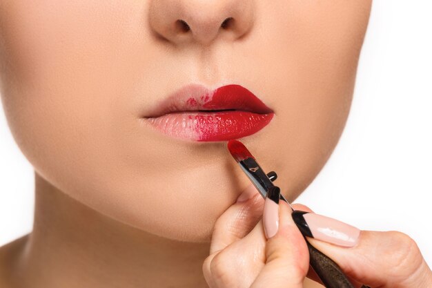 Mooie vrouwelijke lippen met make-up en penseel op wit. Make-up artiest werkproces