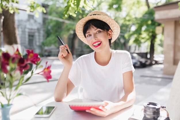 Mooie vrouwelijke student die in tuin met notitieboekje en pen koelen die bloemsmaak geniet