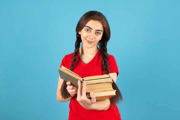 Mooie vrouwelijke student in rood t-shirt die aandachtig boek op blauwe muur leest.