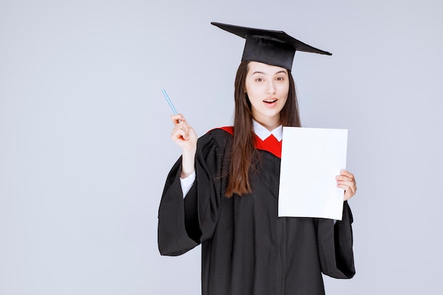 Mooie vrouwelijke student papier en pen in handen poseren met open mond. Hoge kwaliteit foto