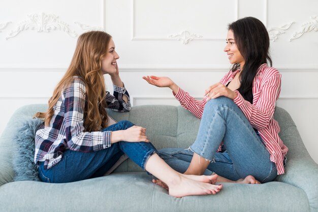 Mooie vrouwen die terwijl het zitten op bank babbelen