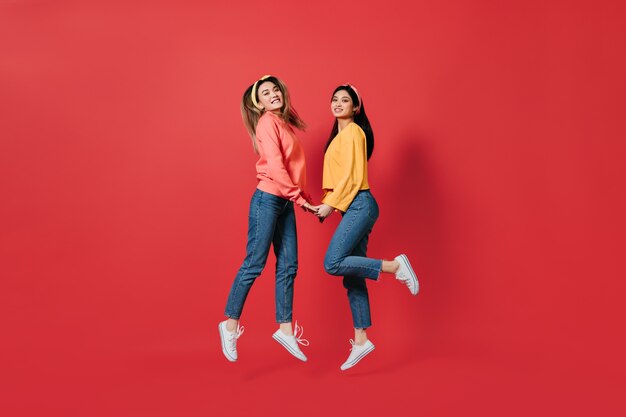 Mooie vrouwen in stijlvolle sweatshirts en jeans springen op de rode muur