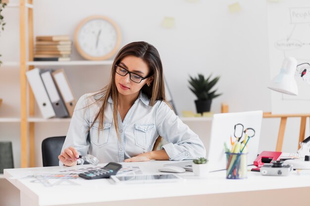 Mooie vrouwenzitting op kantoor en holding een vergrootglas