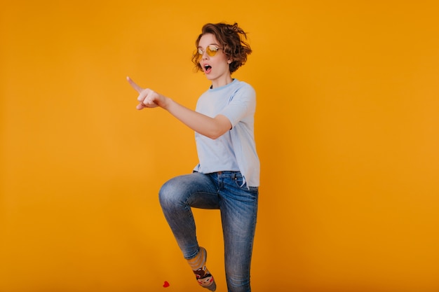 Gratis foto mooie witte vrouw die in trendy denimbroek op gele ruimte springt