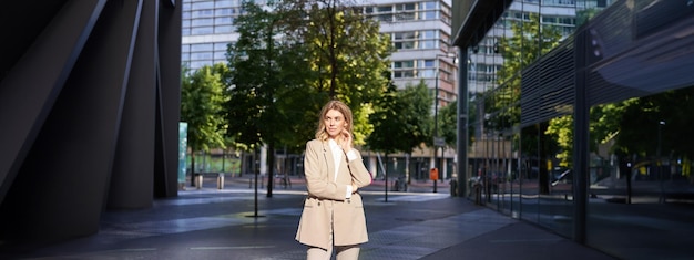 Gratis foto mooie zakenvrouw in beige pak staande in de buurt van kantoorgebouwen op straat poseren met vertrouwen