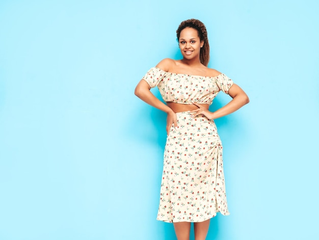 Mooie zwarte vrouw met afro krullen kapsel glimlachend model gekleed in zomerjurk Sexy zorgeloze vrouw poseren in de buurt van blauwe muur in studio gelooid en vrolijk