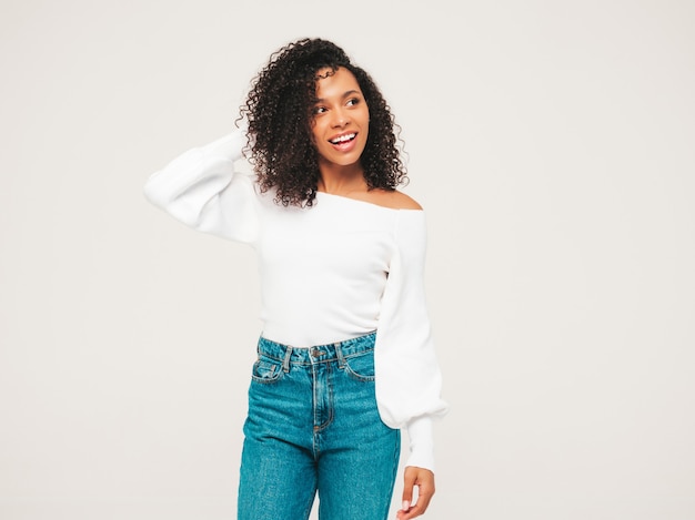 Mooie zwarte vrouw met afro krullen kapsel. Glimlachend model in trui en trendy jeanskleding