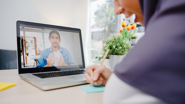 moslim zakenvrouw met behulp van laptop praten met collega over plan door video-oproep brainstorm online vergadering terwijl op afstand werken vanuit huis in de woonkamer.