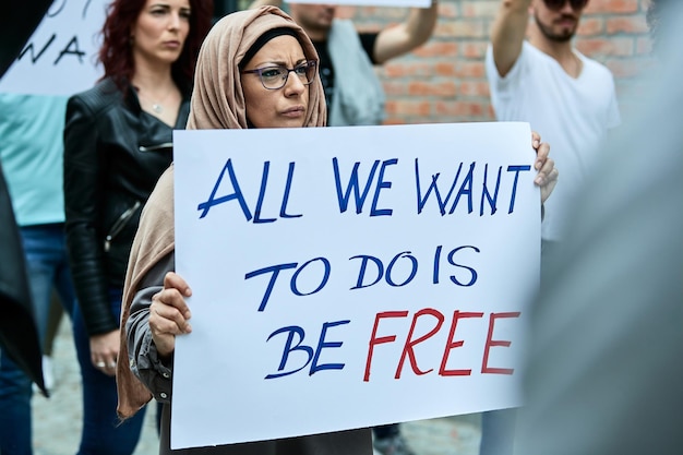 Moslimvrouw die een bordje met vrijheidsinscriptie draagt terwijl ze protesteert met een menigte mensen op straat