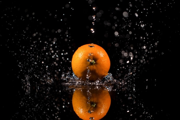 Mousserend water valt op sappige rode oranje die op zwarte tafel staat