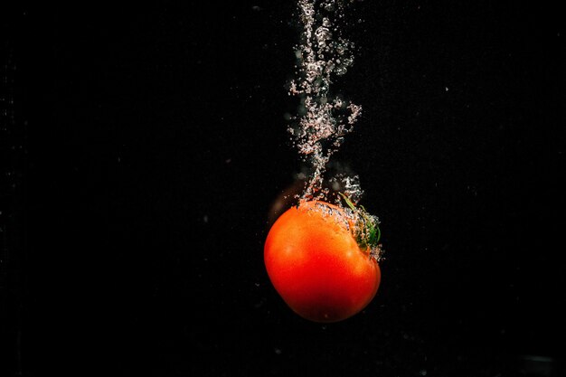 Mousserende rode tomaten vallen in water en spat het